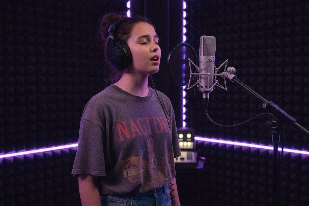 Une adolescente au casque chante devant un grand micro de studio, néons violets dans la cabine