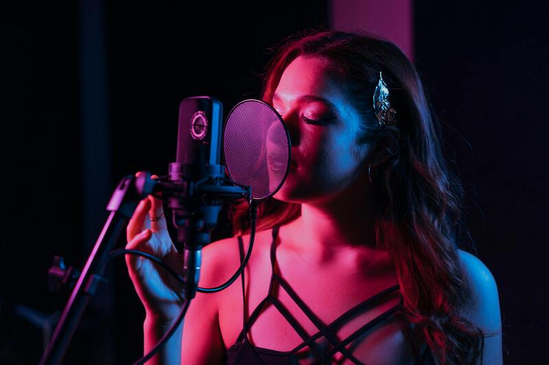 Une chanteuse au micro dans le studio, éclairée en rose et bleu