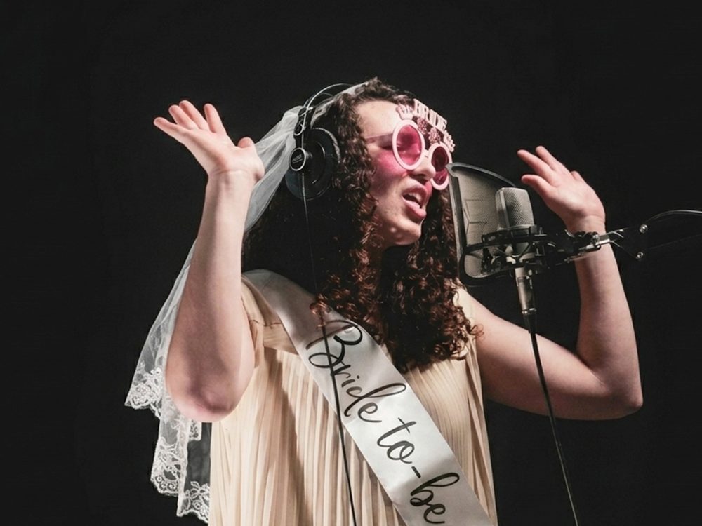 La future mariée chante au micro du studio, voile et écharpe « Bride to be »